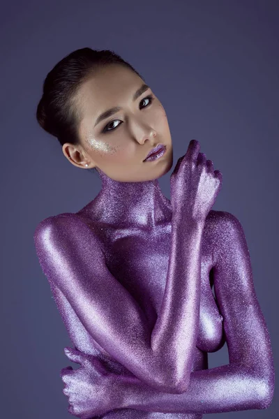 Модная обнаженная азиатка в ультрафиолетовом блеске, изолированная на фиолетовом — стоковое фото