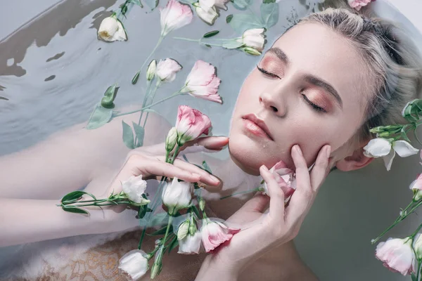Вид зверху красивої жінки, що лежить у воді з закритими очима серед квітів у білій ванні — стокове фото