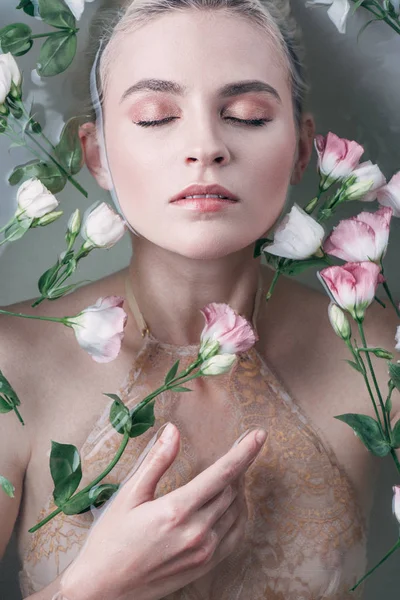 Вид зверху красива мокра жінка в мереживному нижній білизні лежить у чистій воді з квітами і закритими очима в білій ванні — стокове фото