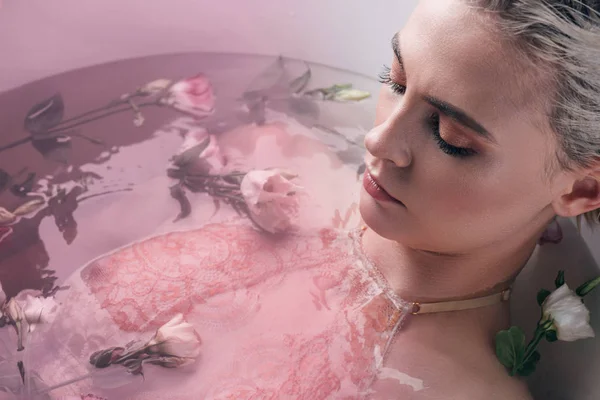 Красива жінка лежить у чистій воді з квітами у білій ванні, рожеве тоноване зображення — стокове фото