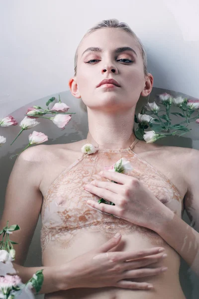 Sexy hermosa mujer acostada en el agua con flores en la bañera blanca — Stock Photo