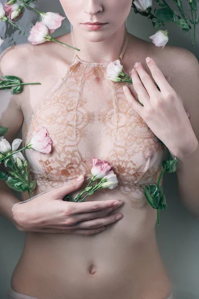 Частковий вид на мокру сексуальну жінку в мереживній білизні, що тримає квіти у воді — стокове фото