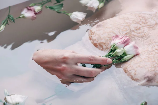 Vista ritagliata di bagnato donna sexy in biancheria intima di pizzo che tiene fiori in acqua — Foto stock