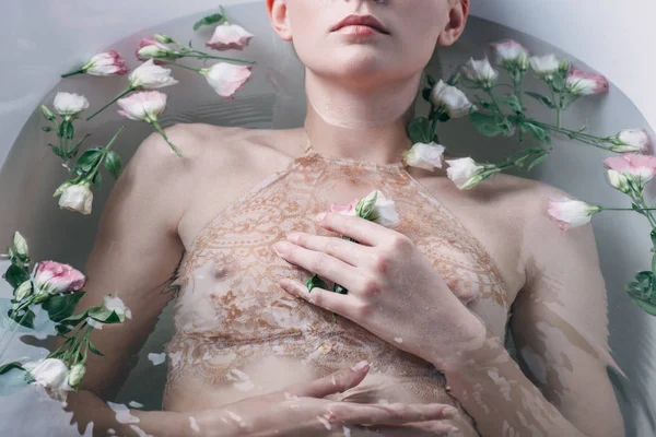 Vista parziale di bella donna sdraiata in acqua limpida con fiori nella vasca da bagno bianca — Foto stock