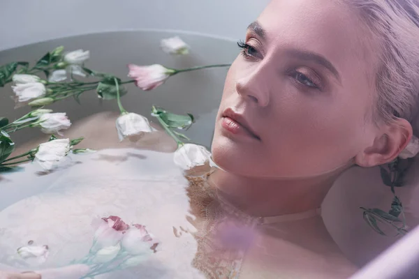 Bela mulher em roupa interior de renda deitada na água com flores na banheira branca — Fotografia de Stock