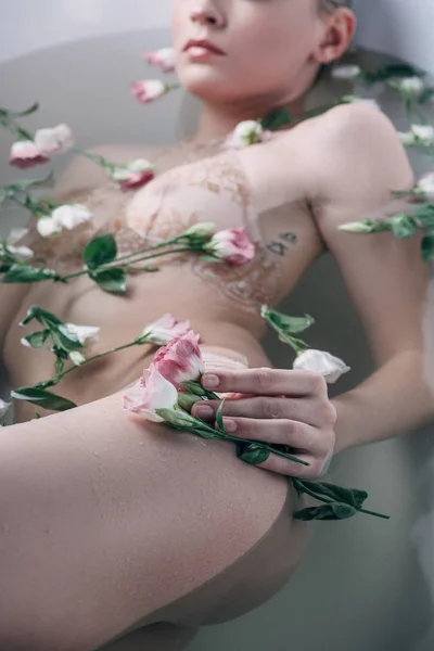 Foco seletivo de mulher sexy deitada em água clara com flores na banheira branca — Fotografia de Stock