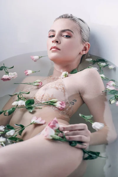 Schöne Frau in beiger Spitzenunterwäsche im klaren Wasser liegend mit Blumen in weißer Badewanne — Stockfoto
