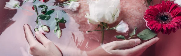 Vista parcial de mujer sexy en lencería beige en agua rosa entre flores, plano panorámico - foto de stock