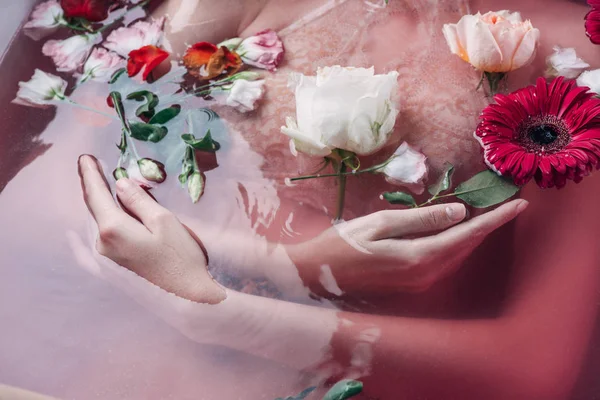 Vista parcial de mujer sexy en lencería beige en agua rosa entre flores - foto de stock