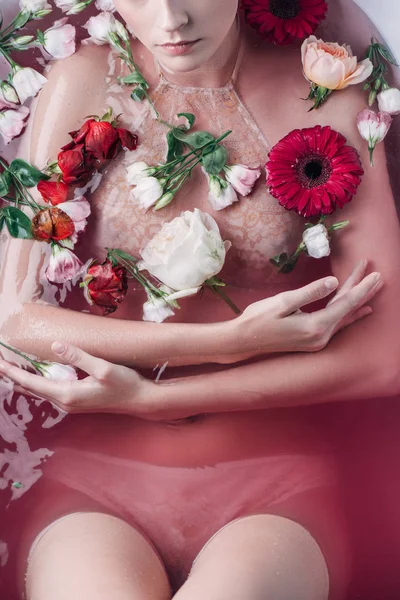 Vista recortada de mujer sexy en lencería beige en agua rosa entre flores - foto de stock