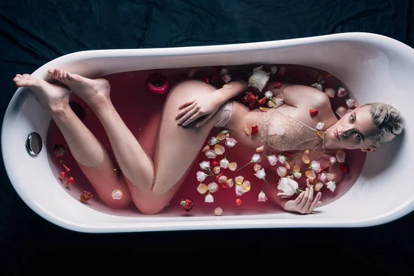 Vista superior da mulher sexy em lingerie bege na banheira com água rosa e pétalas — Fotografia de Stock
