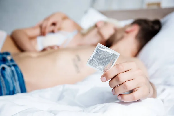 Foco seletivo do homem sem camisa segurando preservativo na cama — Fotografia de Stock