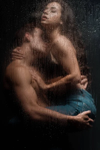 Belo casal apaixonado abraçando atrás de vidro molhado — Fotografia de Stock