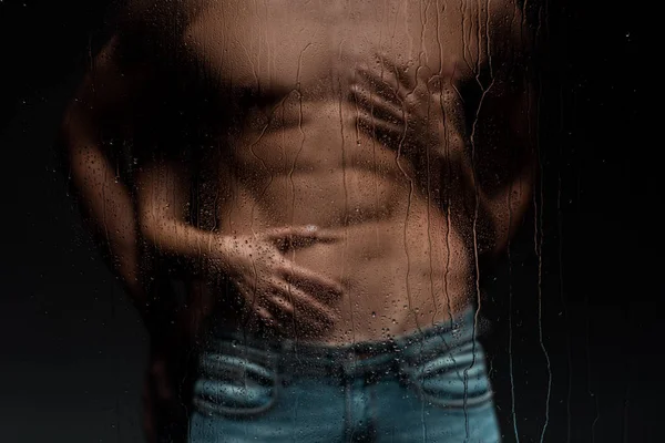 Vista recortada de la mujer seductora abrazando hombre sin camisa detrás de vidrio húmedo - foto de stock