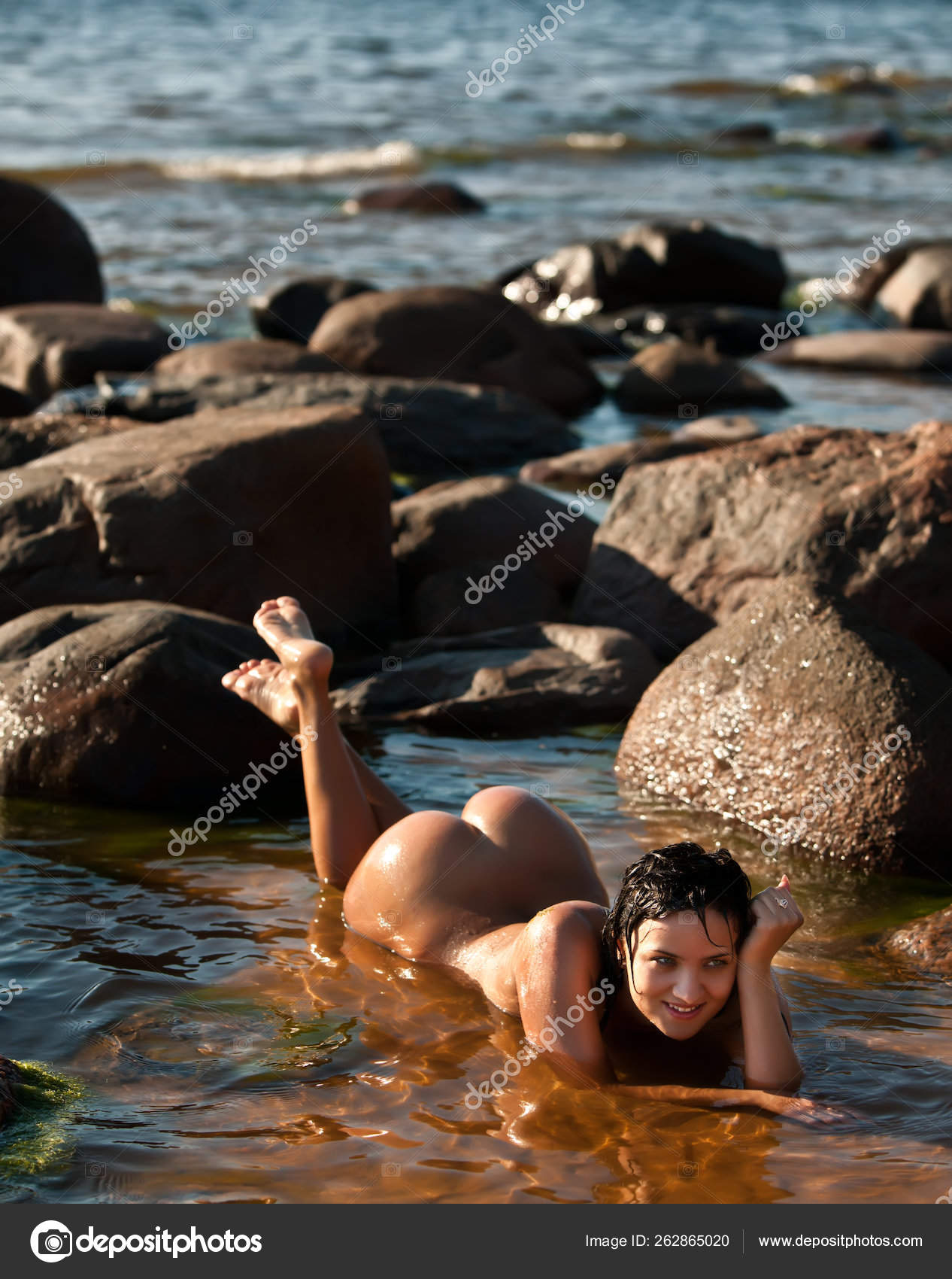 Молодая обнаженная женщина лежит в воде на пляже 