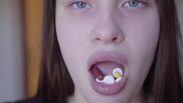 カメラを見て、口の中に多くの錠剤を保持している悪い見た目の女性の顔のクローズアップ。困った十代の若者たち。薬物中毒スローモーション